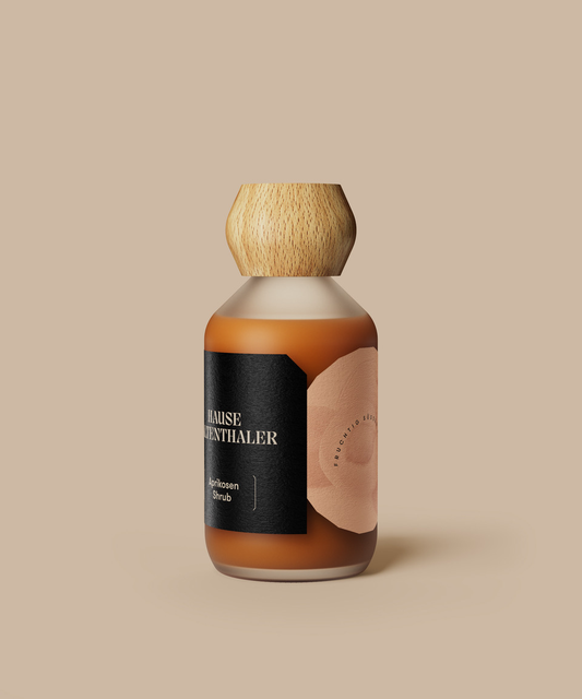 Eine Glasflasche mit Holzdeckel und schwarzem Etikett, die Haus Kaltenthaler APRIKOSEN SHRUB enthält, steht elegant auf einem beigen Hintergrund.