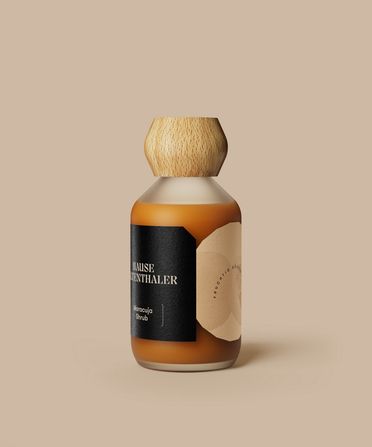 Eine Braunglasflasche mit Holzkappe und minimalistischem Etikett auf beigem Hintergrund, perfekt für die Präsentation des MARACUJA SHRUB von Haus Kaltenthaler oder anderer raffinierter Passionsfrucht-Spezialitäten.