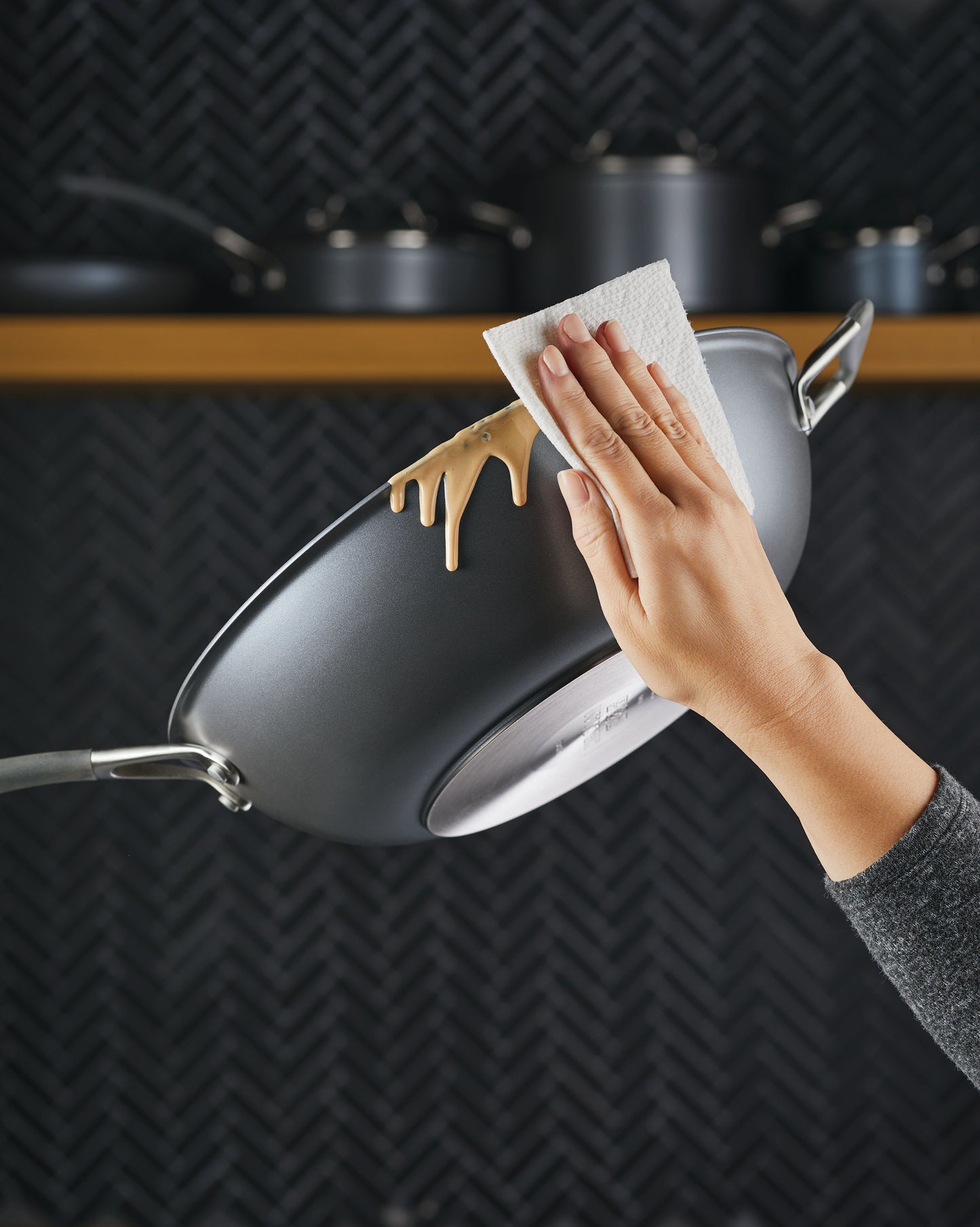 Vor einem dunklen Küchenhintergrund wischt eine Hand mit einem Papiertuch vorsichtig Teig von einer geneigten WOK-PFANNE CIRCULON A1 SERIE 26 cm.