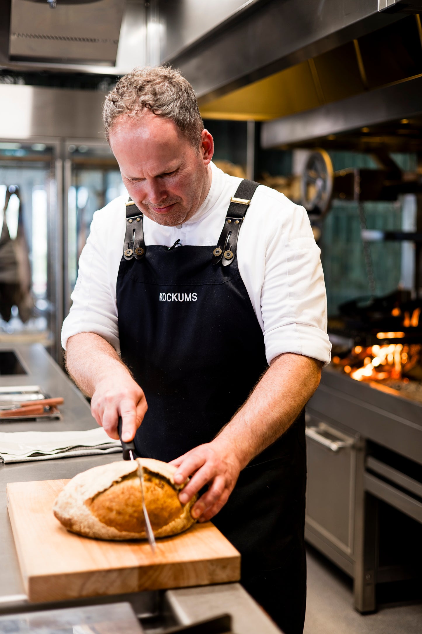 Ein Koch schneidet Brot auf einem langlebigen MASSIVES KÜCHENBRETT AUS SCHWEDEN von Kockums Jernverk in einer professionellen Küche.