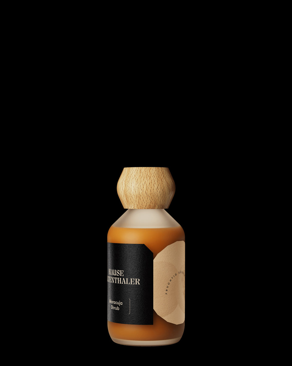Eine Glasflasche mit orangefarbener Flüssigkeit, Holzkappe und schwarzem Etikett mit der Aufschrift Haus Kaltenthaler - perfekt für die Präsentation von MARACUJA SHRUB.