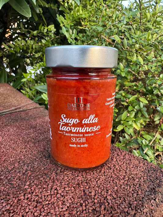 Ein Glas Daidone Sizilianische Taormina Tomatensauce steht auf einem Steinvorsprung, umgeben von üppigem Grün, und erinnert an die reichen Aromen von Passata und sizilianischen Oliven.