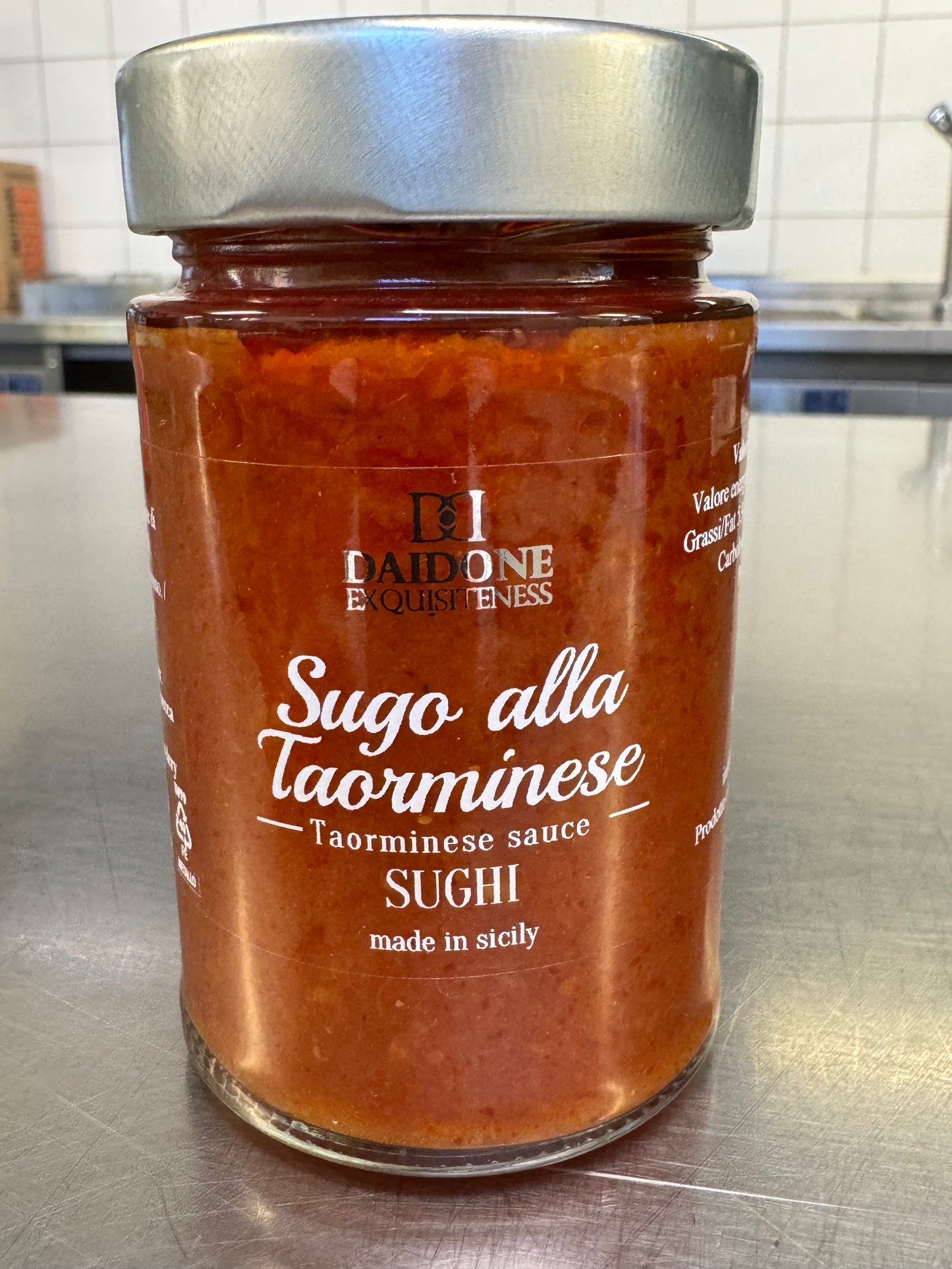 Ein Glas Daidone Sizilianische Taormina Tomatensauce mit Metalldeckel steht auf der Küchentheke. Auf dem Etikett steht „Made in Sicily“. Diese reichhaltige Sauce bringt das Flair Siziliens auf Ihren Tisch.