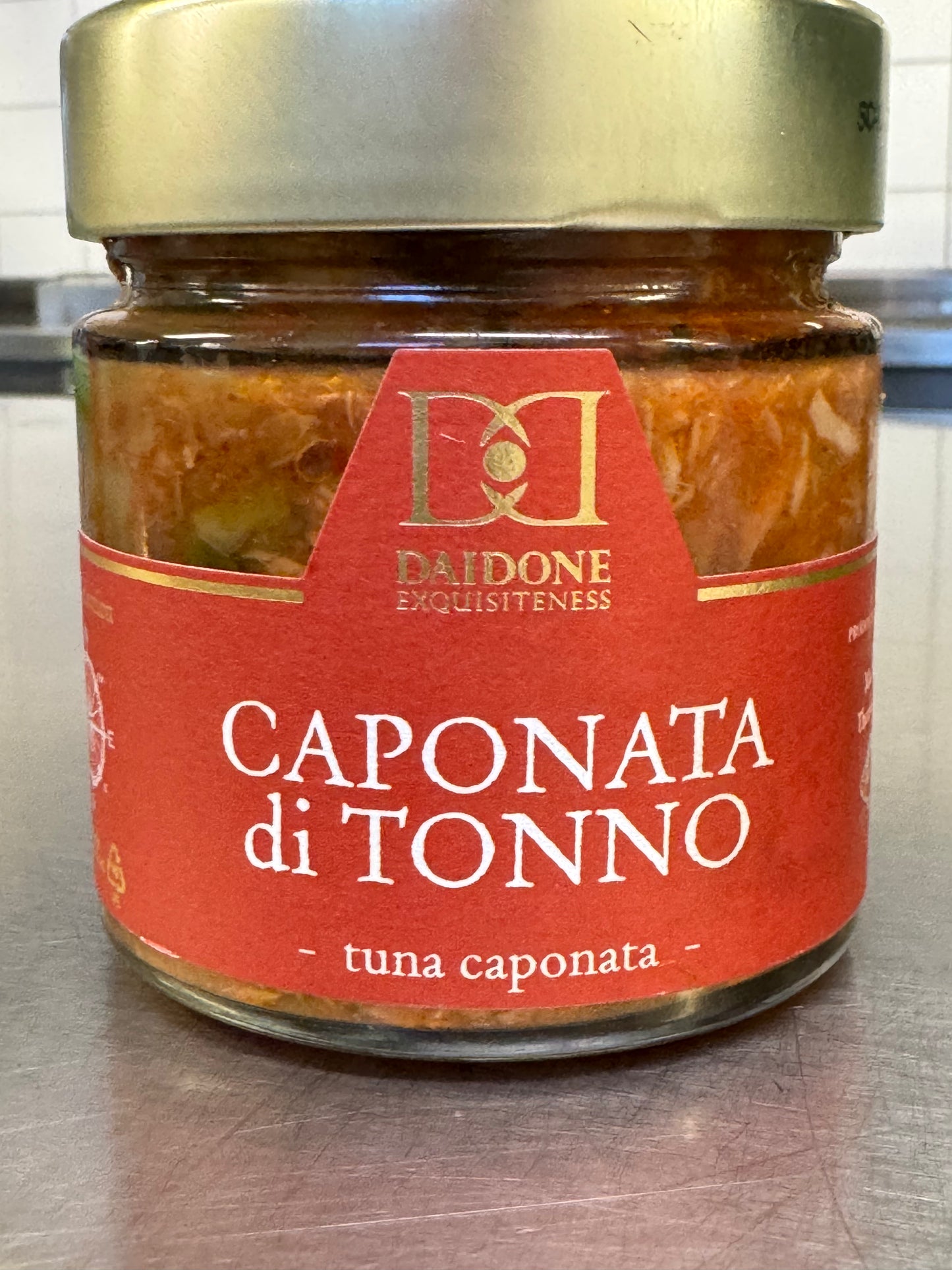 Auf der Küchentheke steht ein Glas „Caponata von Thunfisch und Aubergine“ von Daidone mit rotem Etikett, das die reichen Aromen von Aubergine und Thunfisch perfekt vereint.