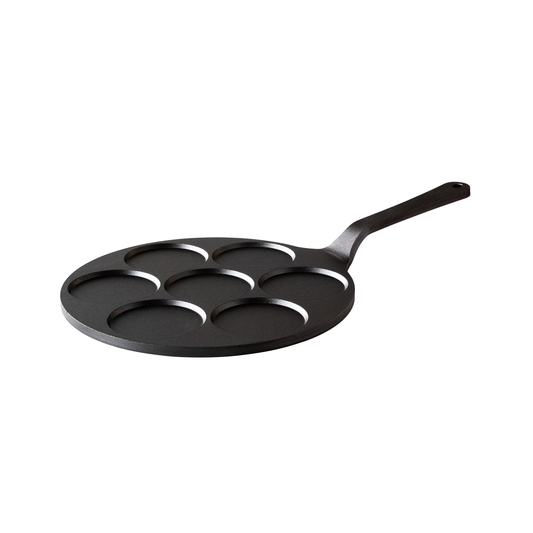 Die Kockums Jernverk MINI-PANCAKE PFANNE KOCKUMS 24 cm ist eine schwarze Kohlenstoffstahlpfanne mit sieben runden Formen und einem langen Griff, ideal für Mini-Pfannkuchen oder Spiegeleier, isoliert auf einem weißen Hintergrund dargestellt.
