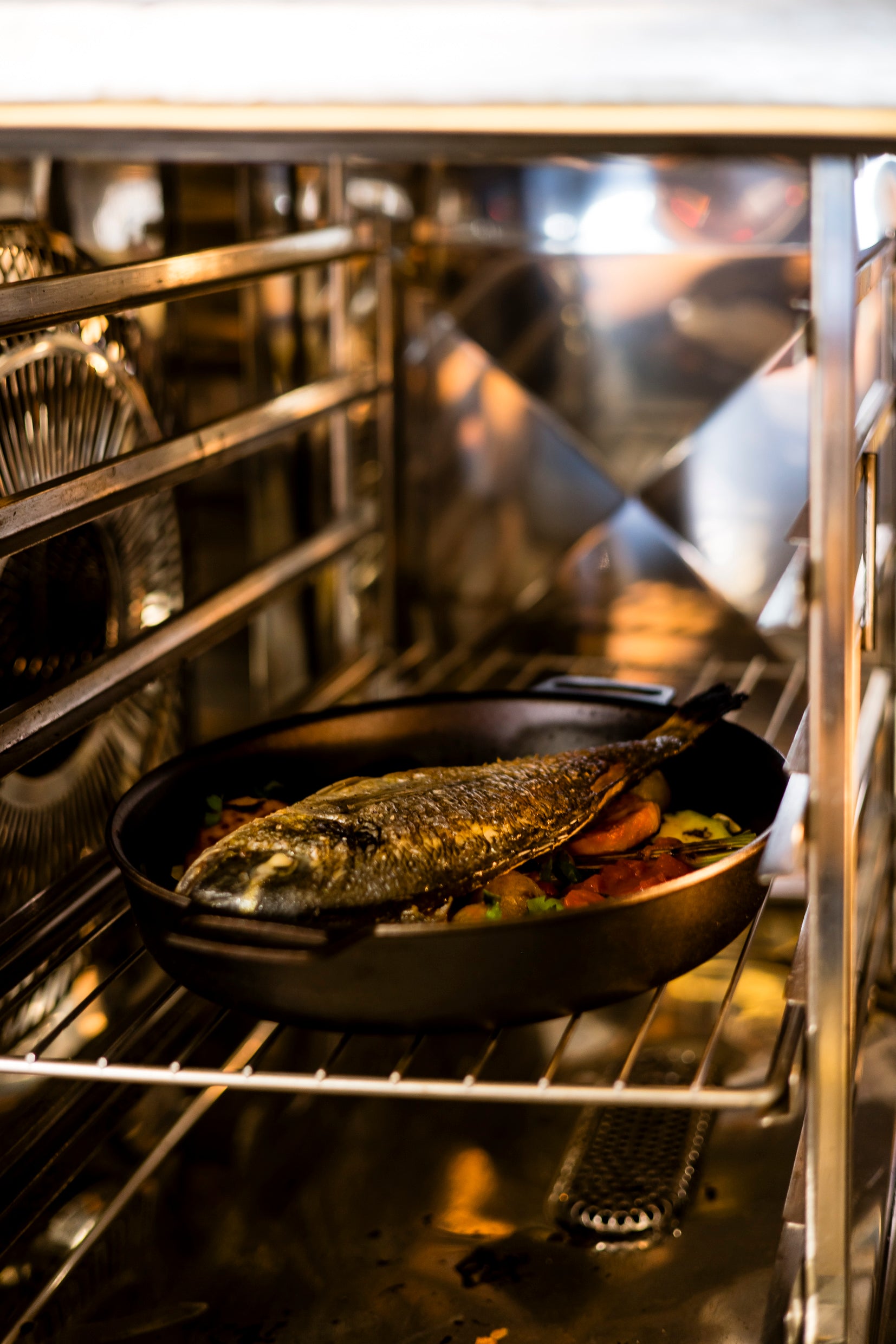 Ein ganzer Fisch wird mit Gemüse in einer 28 cm großen Kockums Jernverk BRATPFANNE-Gusseisenpfanne mit abnehmbarem Griff im Ofen gebraten.
