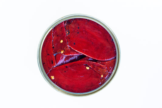 Draufsicht auf geschnittene EINGELEGTE PIQUILLO-PAPRIKA mit Samen, angeordnet in einem runden Glas vor weißem Hintergrund. Marke: El Carrascal.