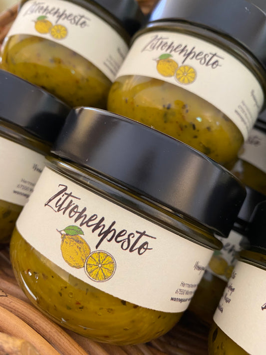 Die Gläser „ZITRONEN PESTO“ der Wonnegauer Ölmühle mit schwarzen Deckeln und zitronenverzierten Etiketten sind ordentlich gestapelt. Dieser köstliche Brotaufstrich vereint Mandelmus und spanische Zitronen und verleiht Ihren kulinarischen Kreationen eine lebendige Note.