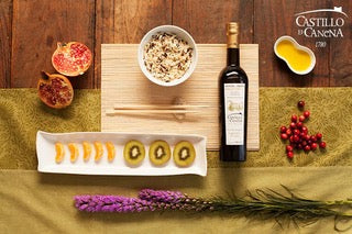 Draufsicht auf eine lebendige Lebensmittelpräsentation mit Reis, Fruchtscheiben, einer Weinflasche und dekorativen Pflanzen, hervorgehoben durch den grünen Tomatengeschmack von OLIVENÖL PICUAL RESERVA FAMILIAR der Agentur für Olivensaft.