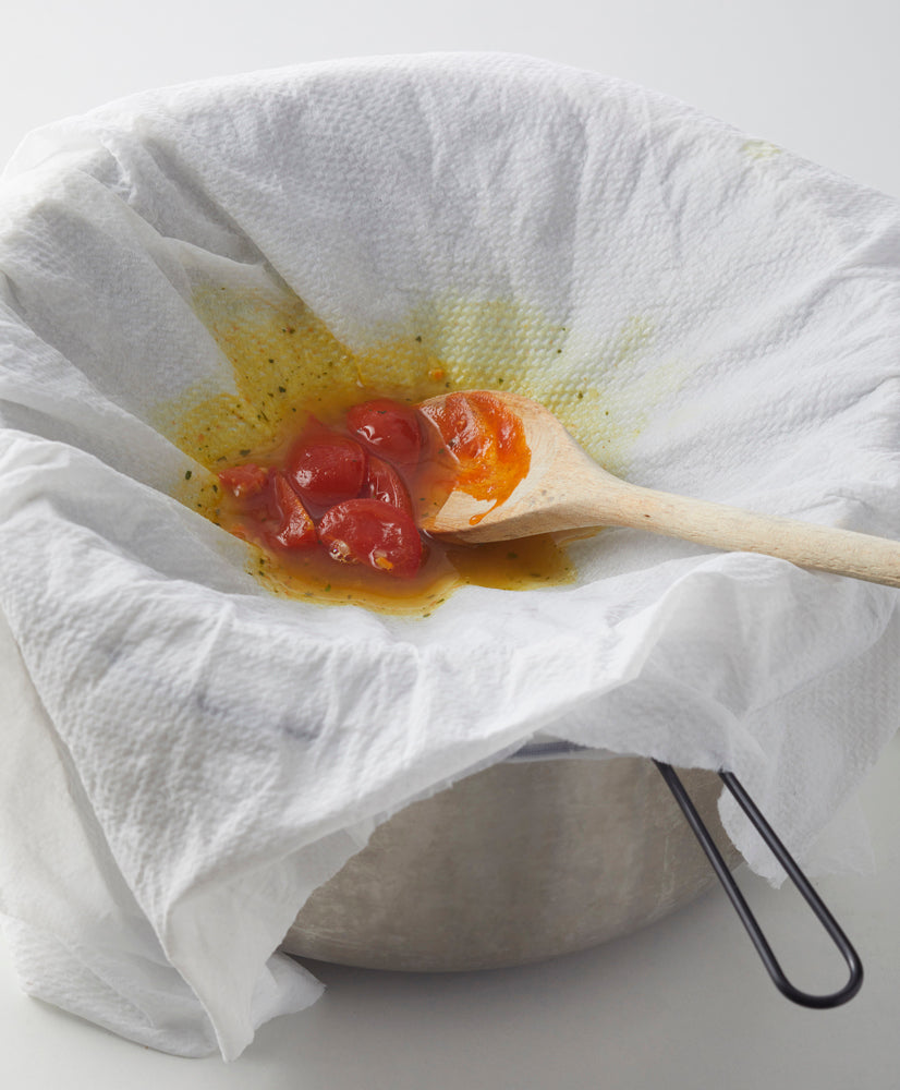 Ein mit Papier ausgelegtes Sieb, gefüllt mit Tomaten und Flüssigkeit und begleitet von einem Holzlöffel, wartet darauf, mit Mensch‘s PASSIERTÜCHER – 3er SET über einem Topf in feine Saucen verwandelt zu werden.