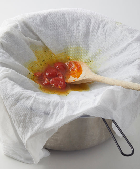 Ein mit Papier ausgelegtes Sieb, gefüllt mit Tomaten und Flüssigkeit und begleitet von einem Holzlöffel, wartet darauf, mit Mensch‘s PASSIERTÜCHER – 3er SET über einem Topf in feine Saucen verwandelt zu werden.