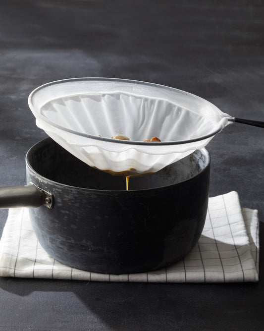 Ein schwarzer Topf mit Griff steht auf einem Tuch und filtert die Flüssigkeit im Inneren mit dem Better Food PASSIERSIEB in verschiedenen Größen, ideal für die Zubereitung zarter, feiner Saucen.