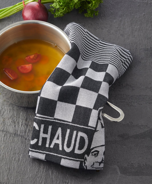 Ein Topf Suppe mit Tomaten, teilweise bedeckt mit einem karierten PREMIUM KÜCHENTUCH von Le Chaud devant, steht neben frischen Kräutern und einer roten Zwiebel.