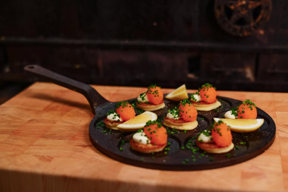 Kleine Blinis mit Sahne, Rogen, Schnittlauch und Zitronenspalten werden auf der Kockums Jernverk MINI-PANCAKE PFANNE 24 cm auf einem Holzbrett serviert.