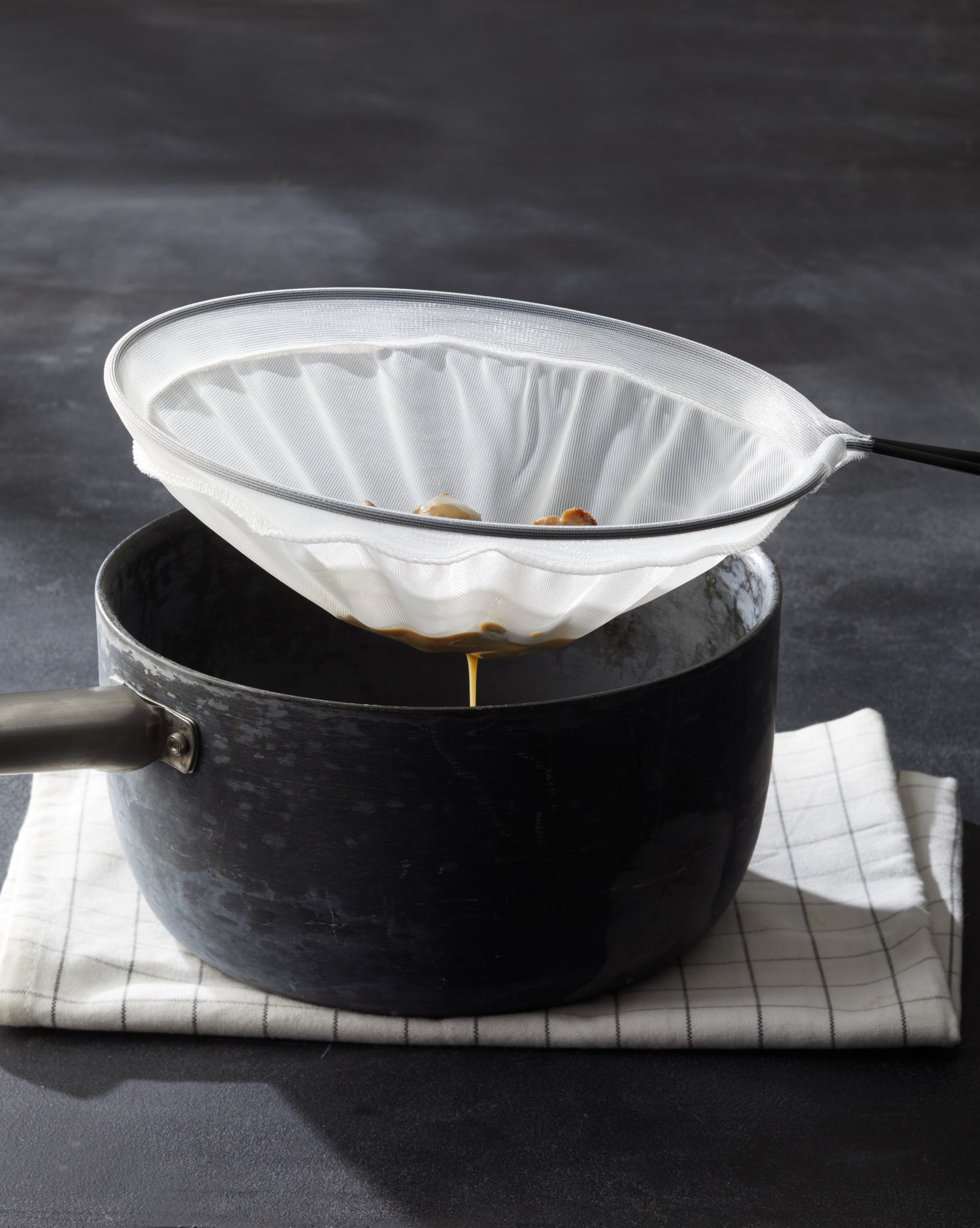 Ein schwarzer Topf mit Griff steht auf einem Tuch und filtert die Flüssigkeit im Inneren mit dem Better Food PASSIERSIEB in verschiedenen Größen, ideal für die Zubereitung zarter, feiner Saucen.