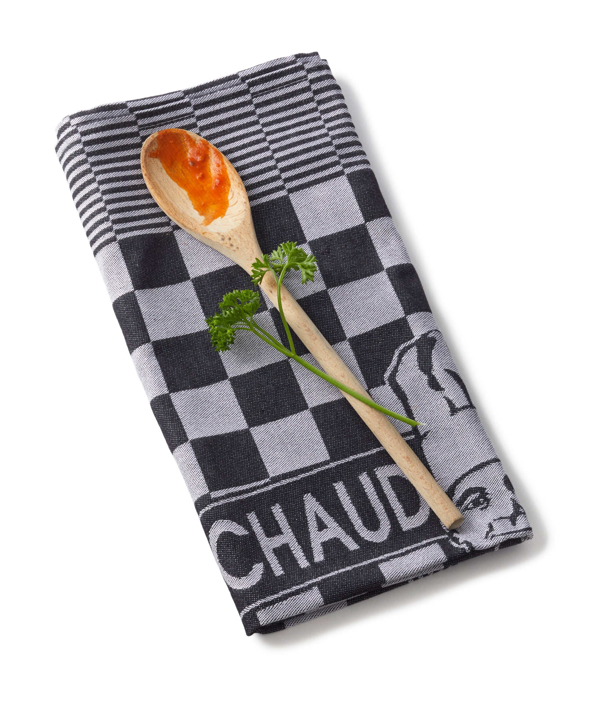 PREMIUM KÜCHENTUCH - PROFIKÜCHEN-TORCHON von Le Chaud devant, begleitet von einem Holzlöffel mit Sauce und garniert mit einem Zweig Petersilie.